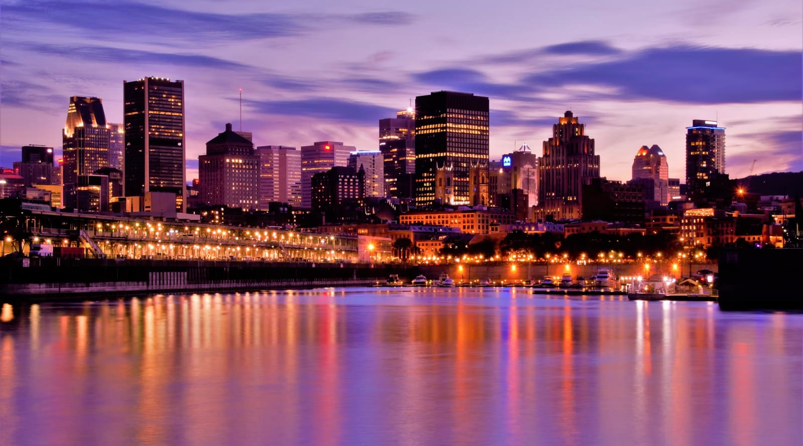 The Montréal skyline at dusk, its lights reflected in the water of the Old Port